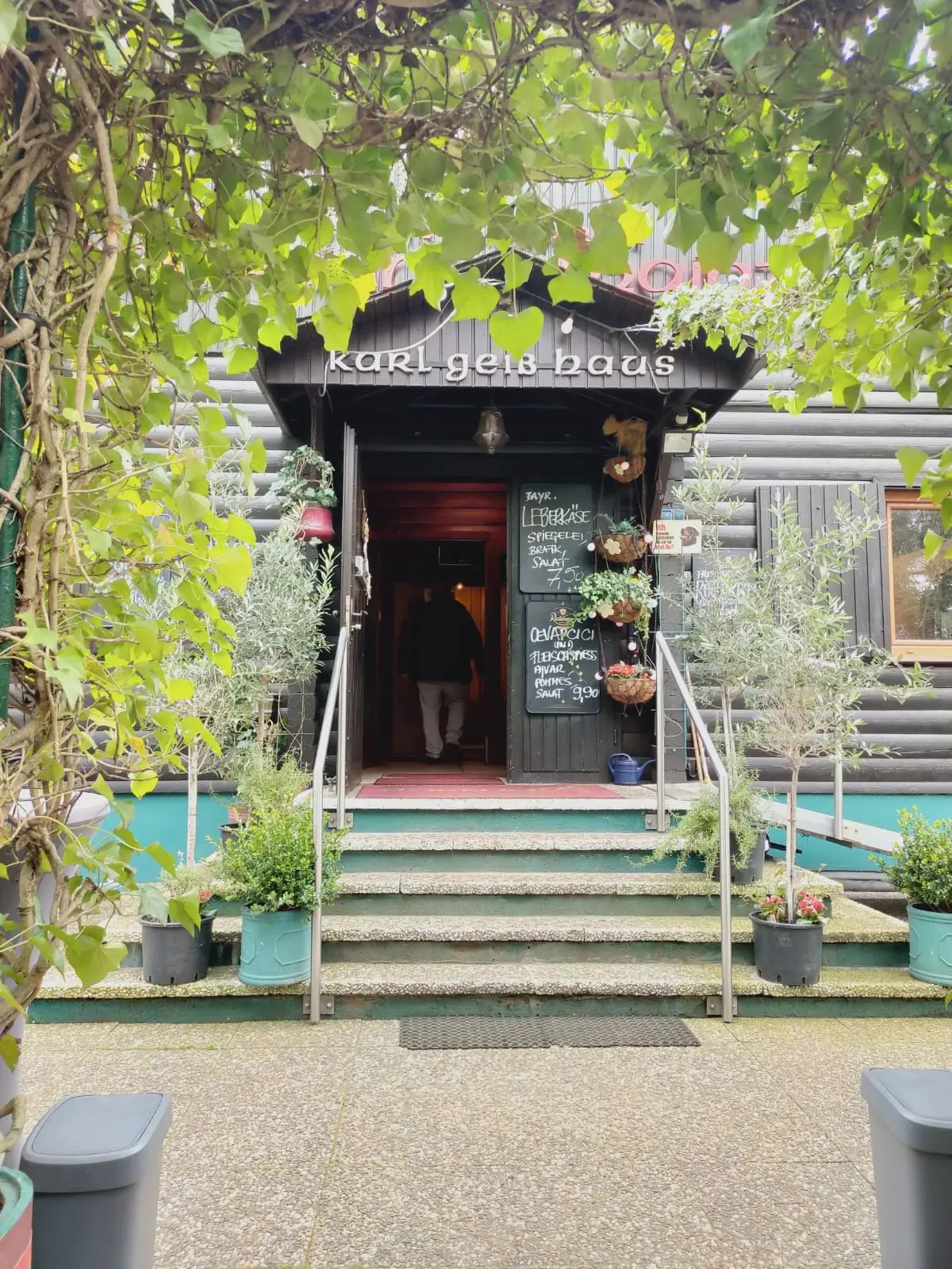 Eingang des Wanderheims: Treppe mit Blumen, darüber das Schild „Karl Geib Haus“