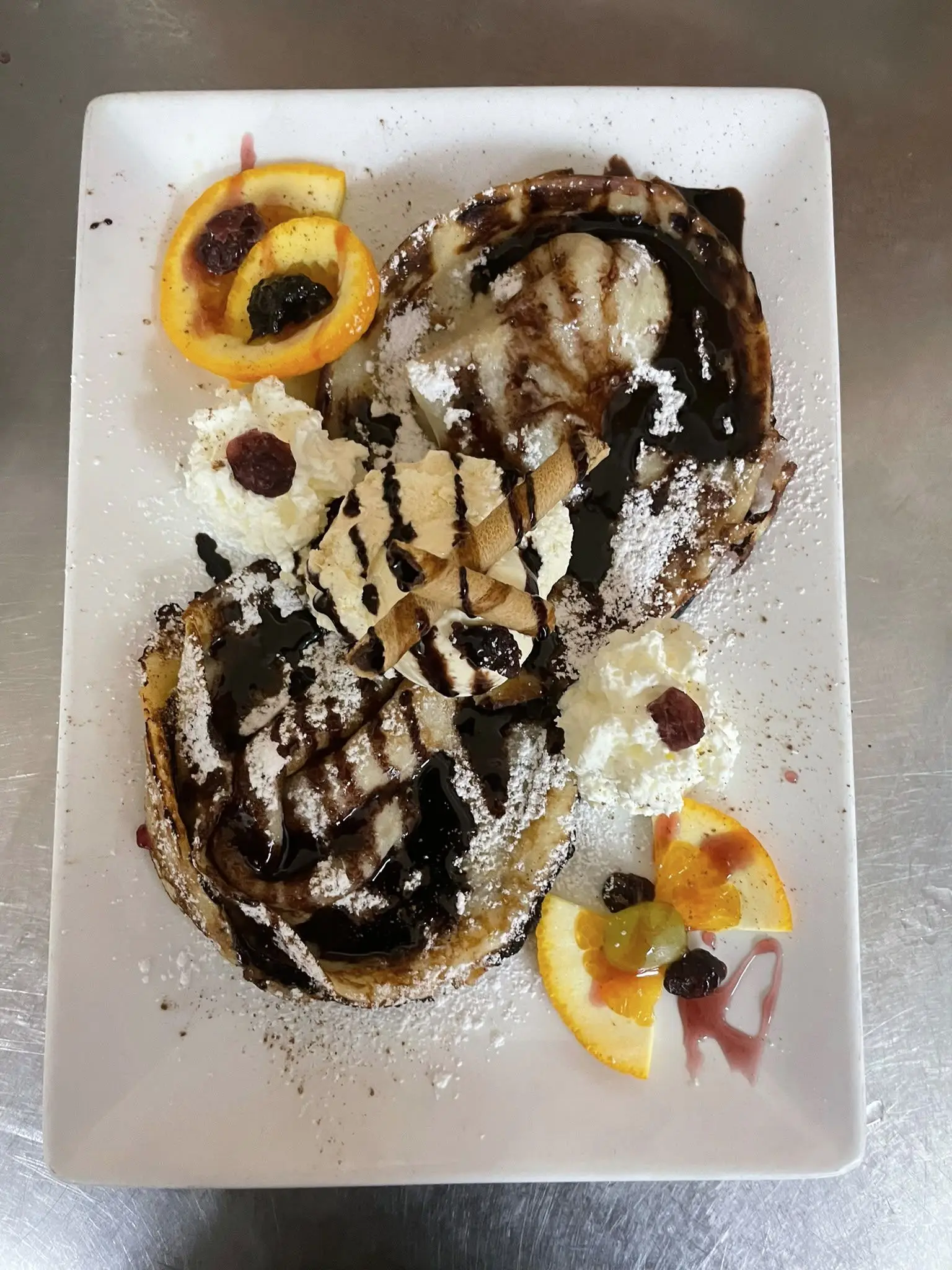 Zwei Palatschinken mit Schokosauce, Puderzucker, Sahne und Orangenscheiben