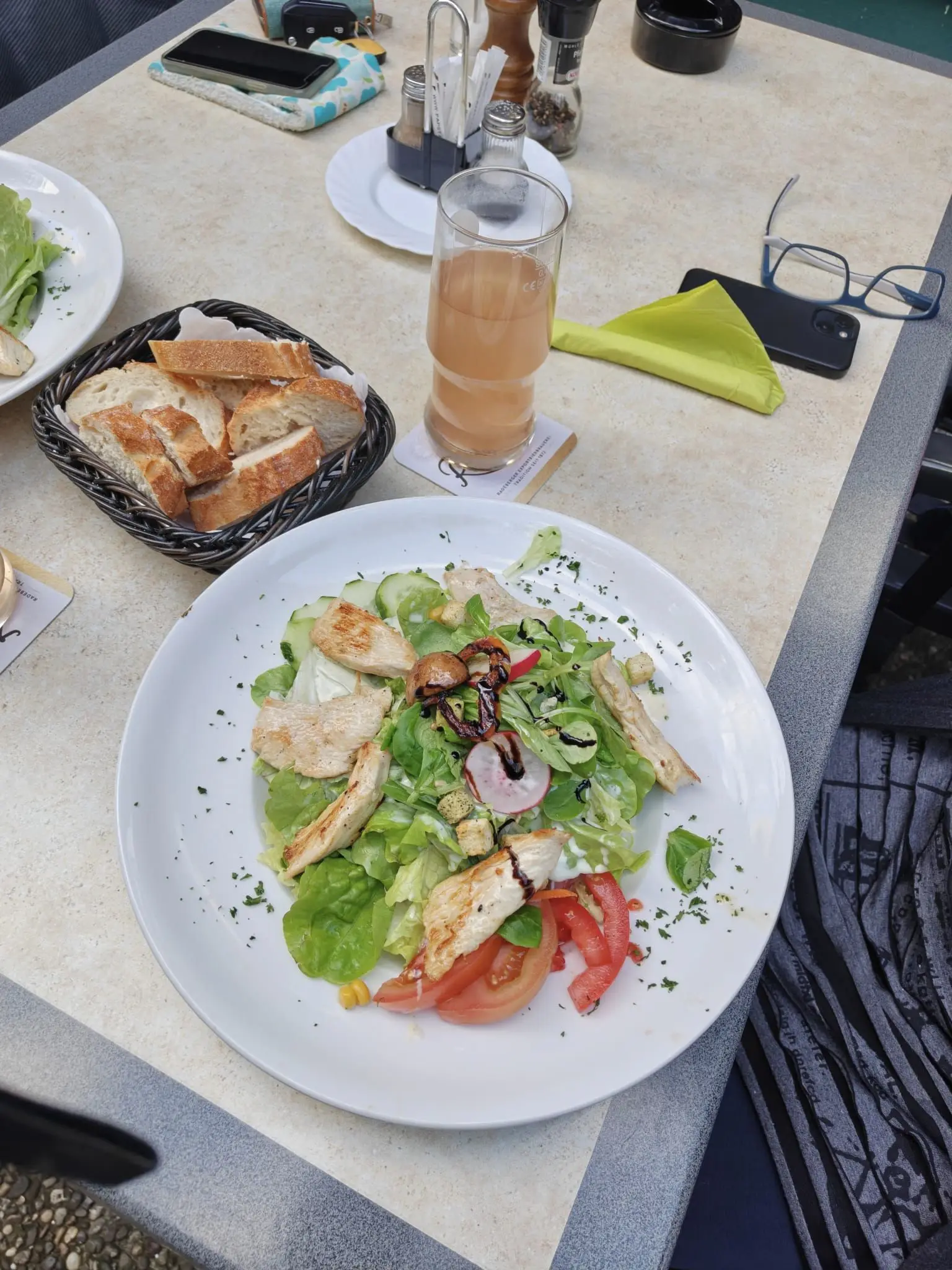 Großer Salatteller mit Hähnchenbrust, Tomaten und Radieschen, daneben ein Brotkorb